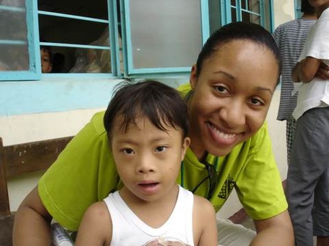 A volunteer sits with a child outside a clinic building.